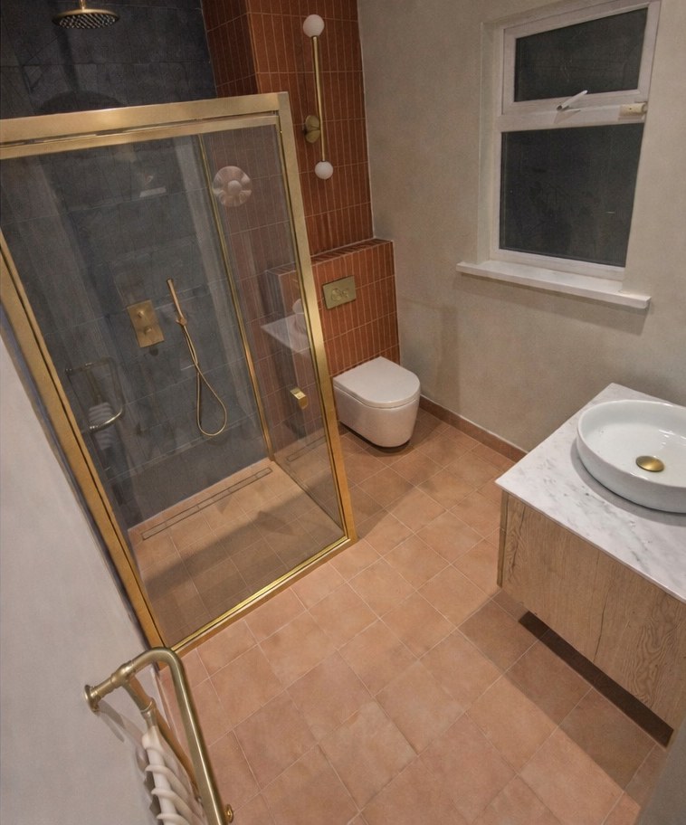The same bathroom after full renovation with walk-in shower and gold fittings